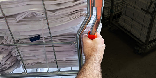 Hand pushing a roll cage full of folded white linen