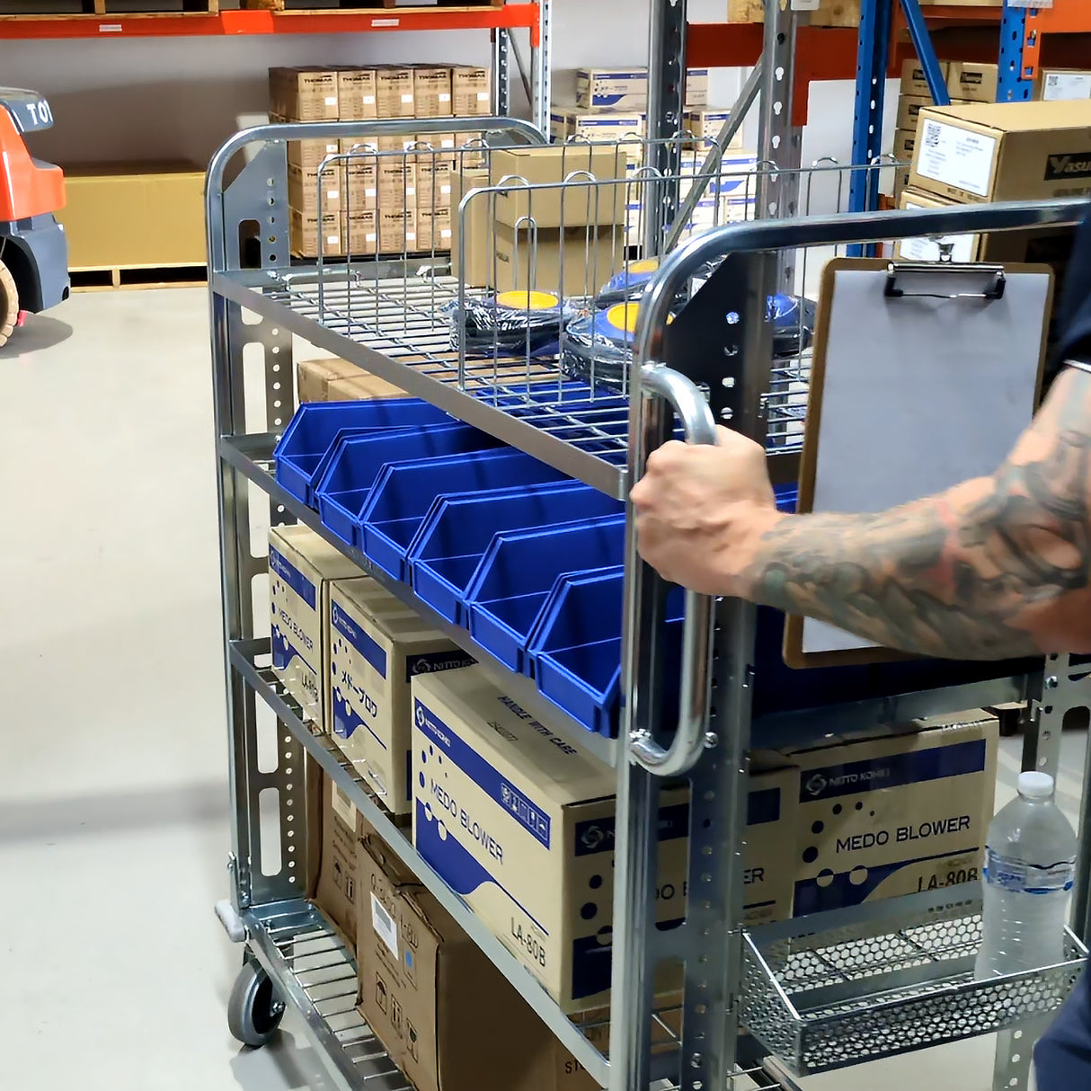 Person pushing a TRS02 with blue storage bins and boxes in a warehouse setting