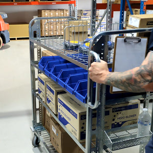 Person pushing a TRS02 with blue storage bins and boxes in a warehouse setting
